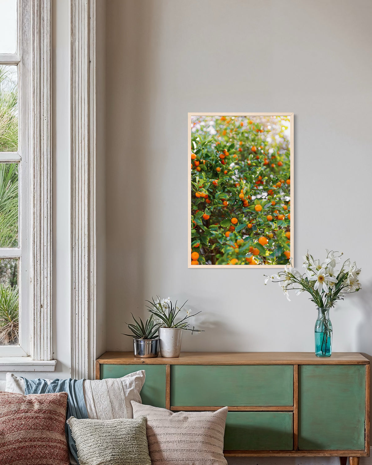 Framed Citrus Summer photo displayed above a green sideboard with leafy plants and white flowers in a cozy room.