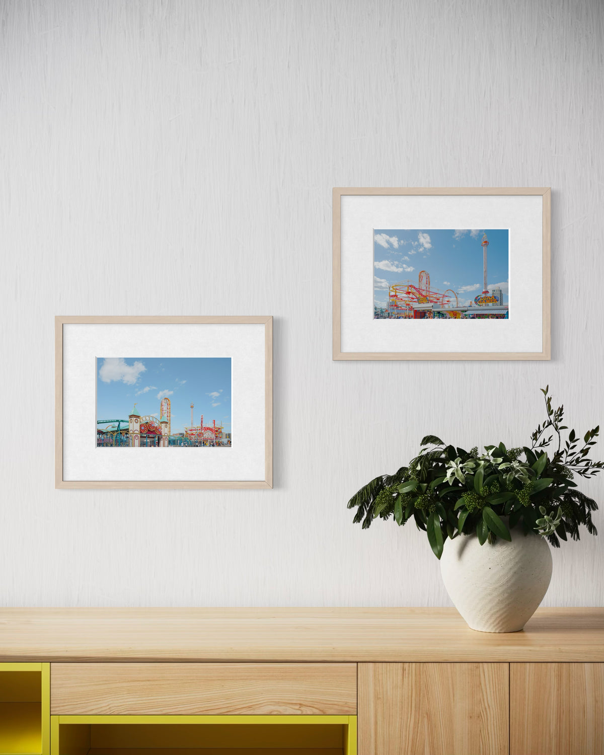 Two Coney Island photographs in black frames hang on a white wall above a cabinet with a potted plant.