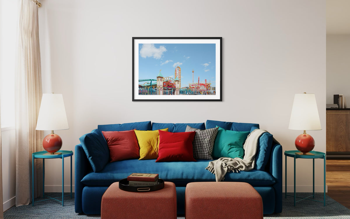 Framed “Coney Island Thunderbolt” photograph on wall above blue sofa with colorful pillows in living room.