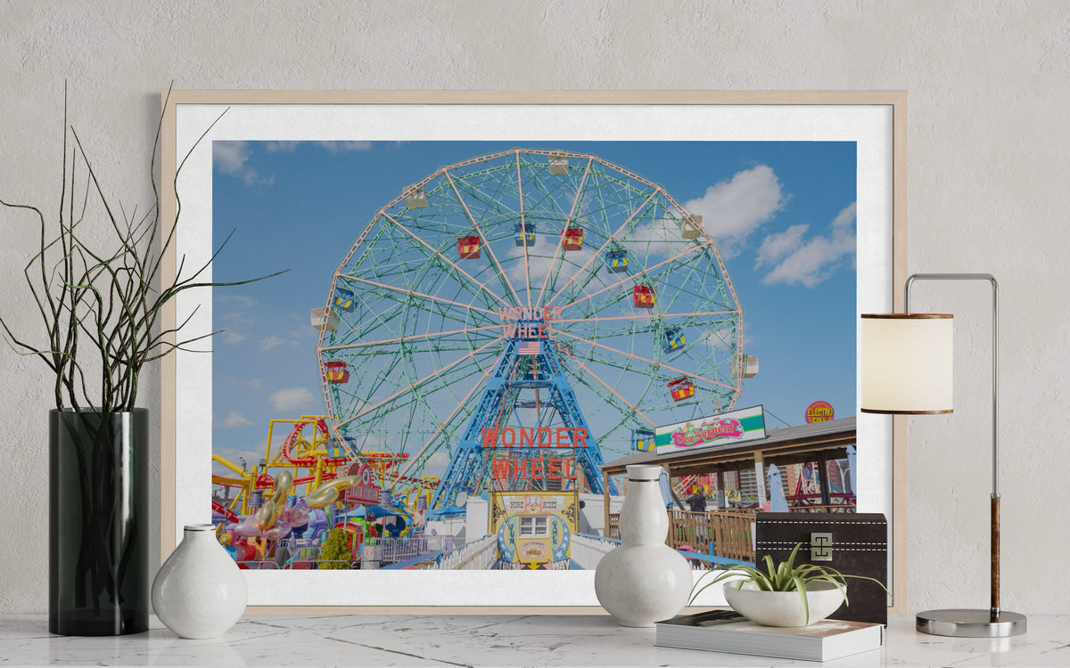Framed photo of the Wonder Wheel at Coney Island displayed on a marble table with vases, books, and a lamp.