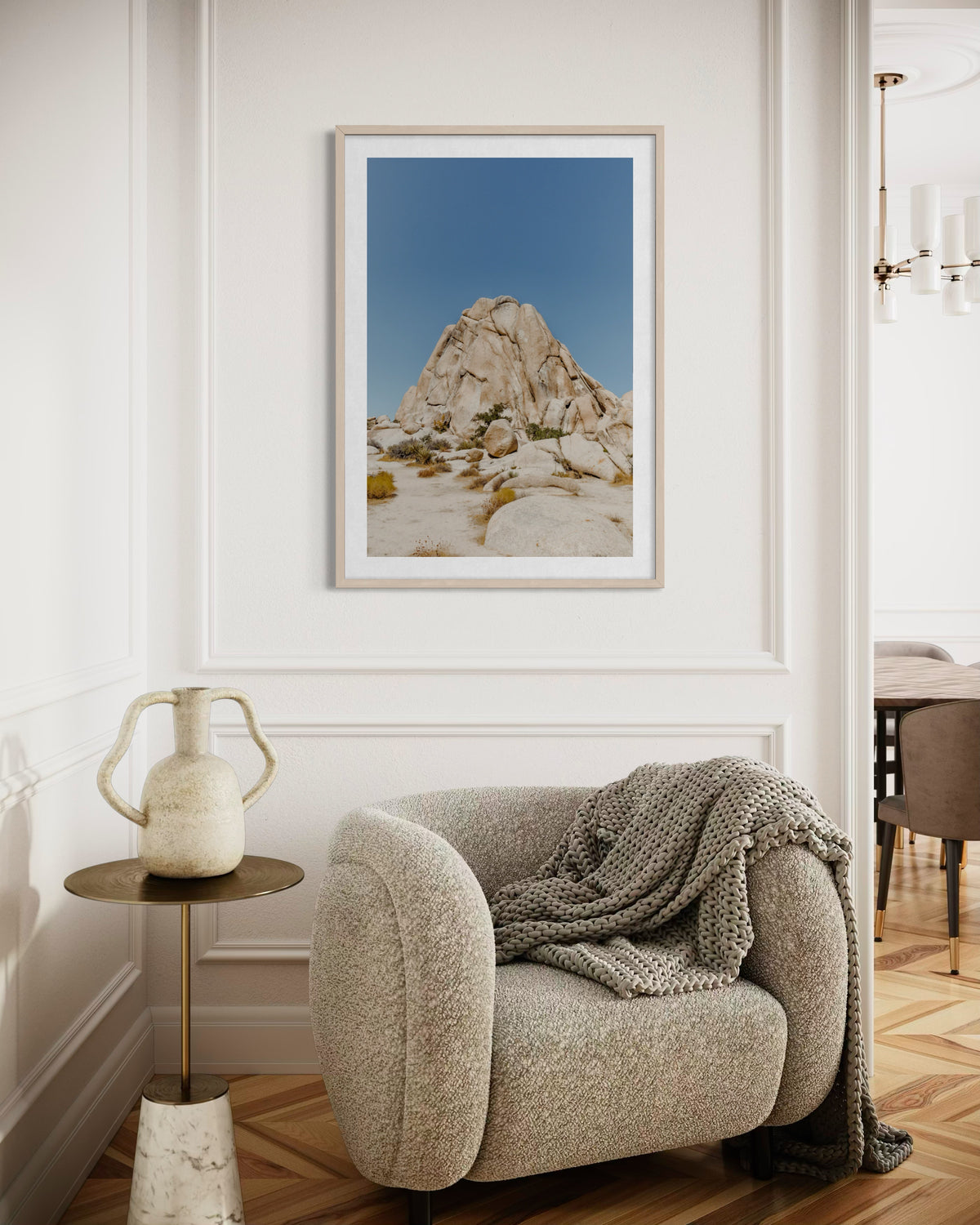Framed “Desert Form” photo on a white wall above a beige chair, blanket, and small table in a modern room.