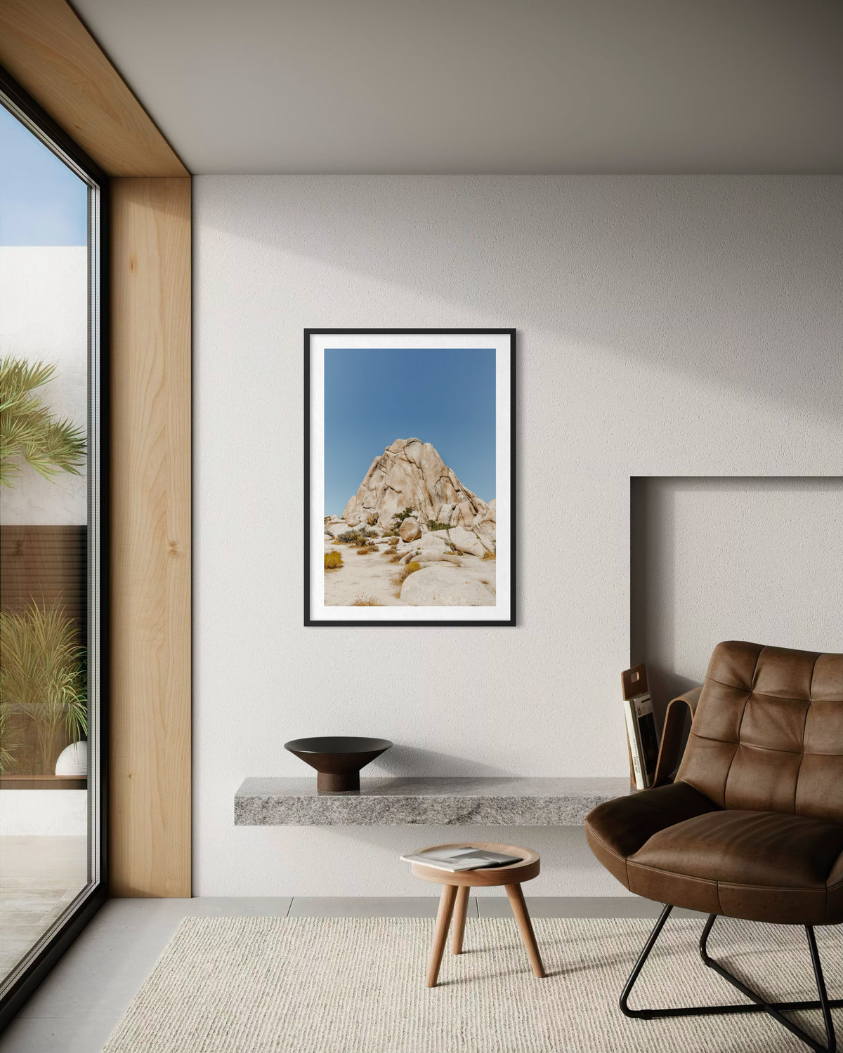 Framed “Desert Form” photo displayed above a leather chair in front of a large window in a living room.