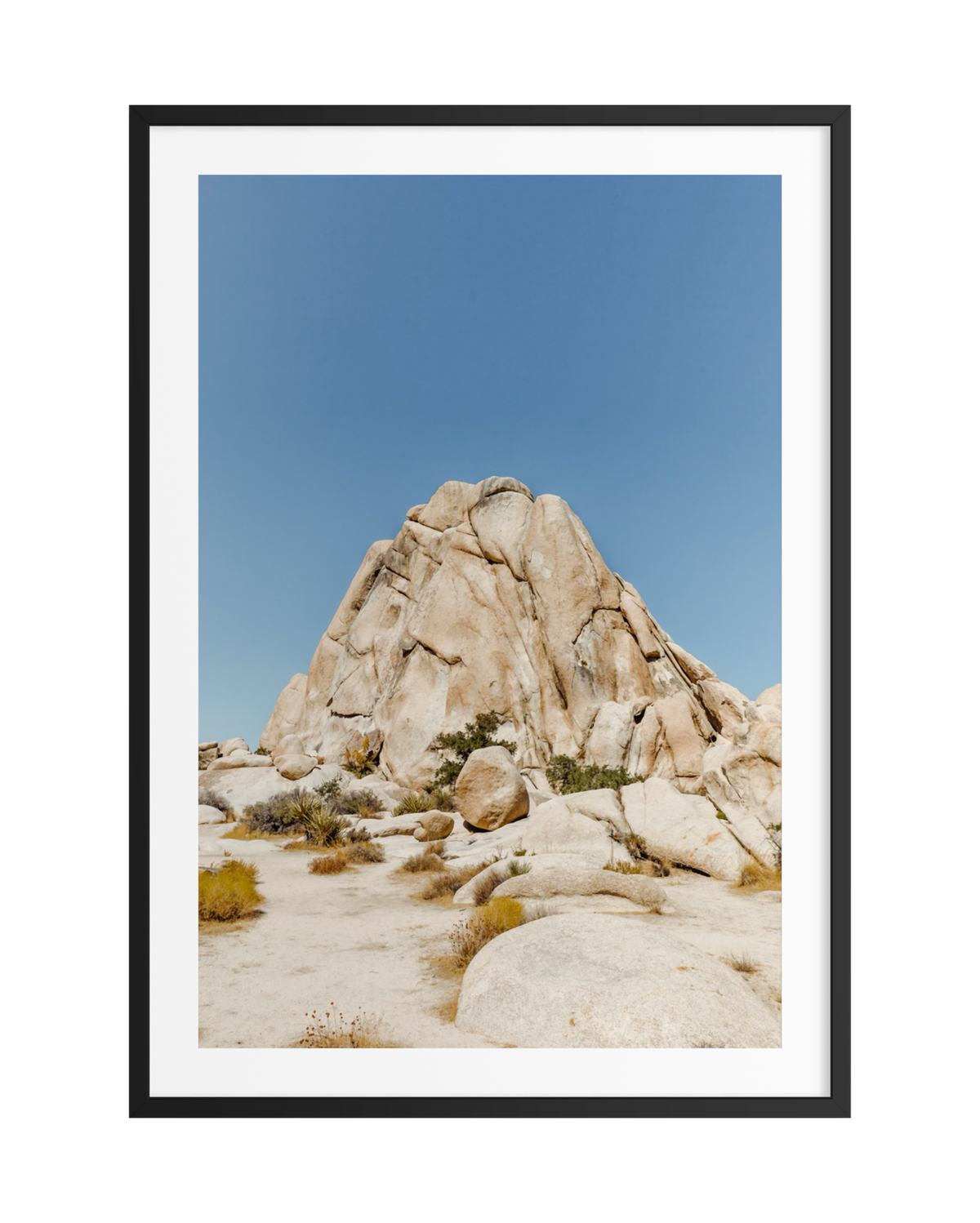 A lone rock rises from sandy desert dotted with shrubs, shown in a black frame.