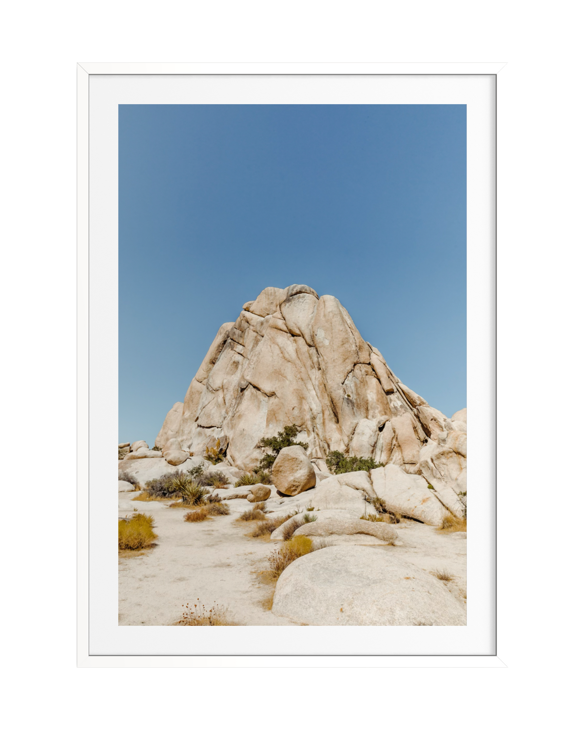 Large tan boulder under clear blue sky with sparse desert plants, shown in a white frame.