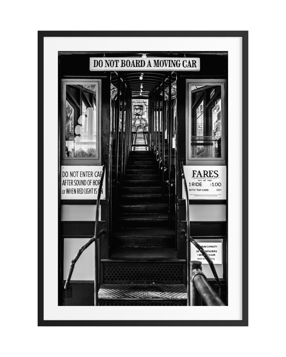 Black and white view of DTLA Funicular Passage stairs, fare signs, and downtown Los Angeles in the distance.