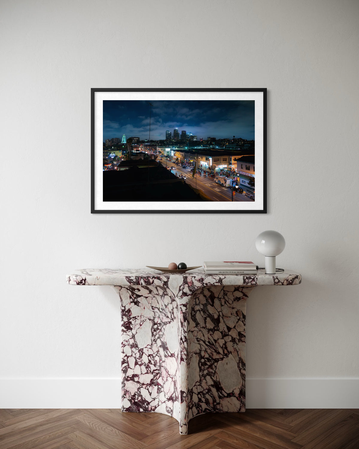 Framed “DTLA Nights” print hangs above a marble console with a lamp against a plain wall.