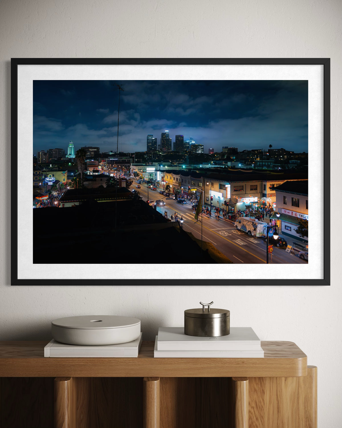 Framed photograph of downtown Los Angeles at night, displayed above a wooden sideboard in a modern room.