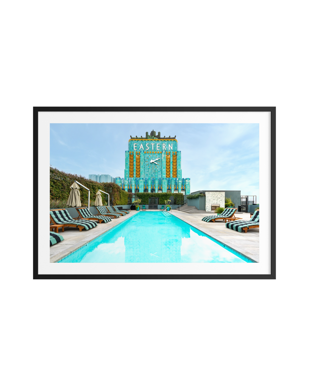 Rooftop pool with striped loungers in front of the Eastern Columbia Building’s Art Deco facade in Los Angeles.