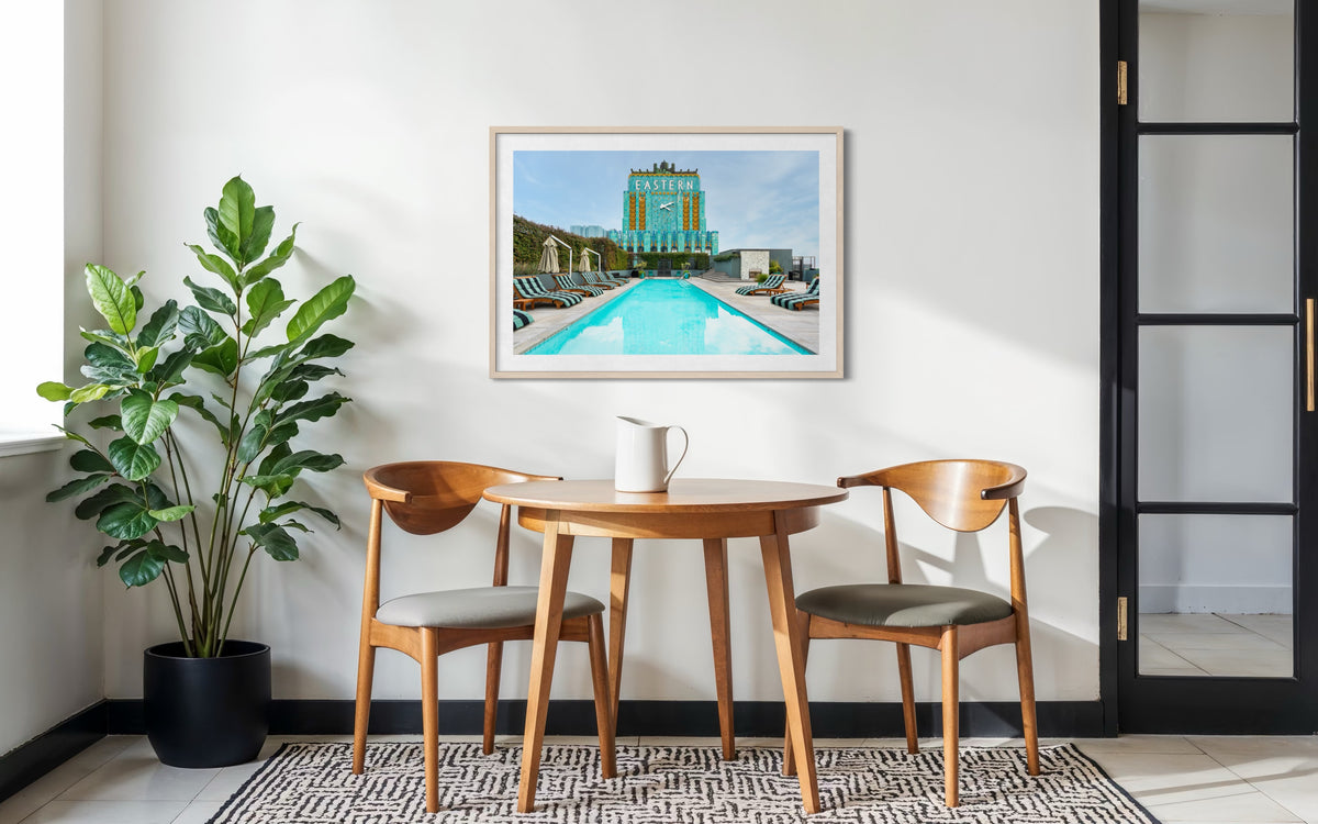 Two chairs and a round table with a plant, beneath Eastern Columbia Building art in a Los Angeles room.