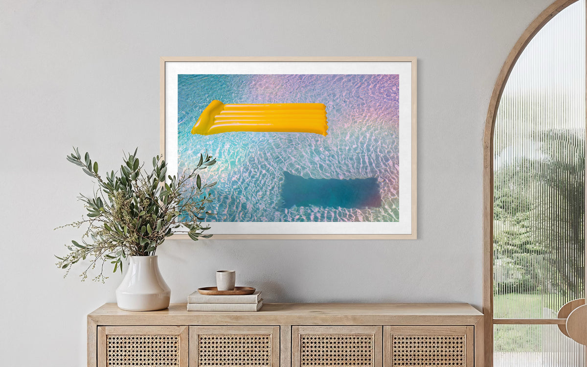 Framed “Floating Through Summer” print from the Refractions Collection displayed above a sideboard with green branches.