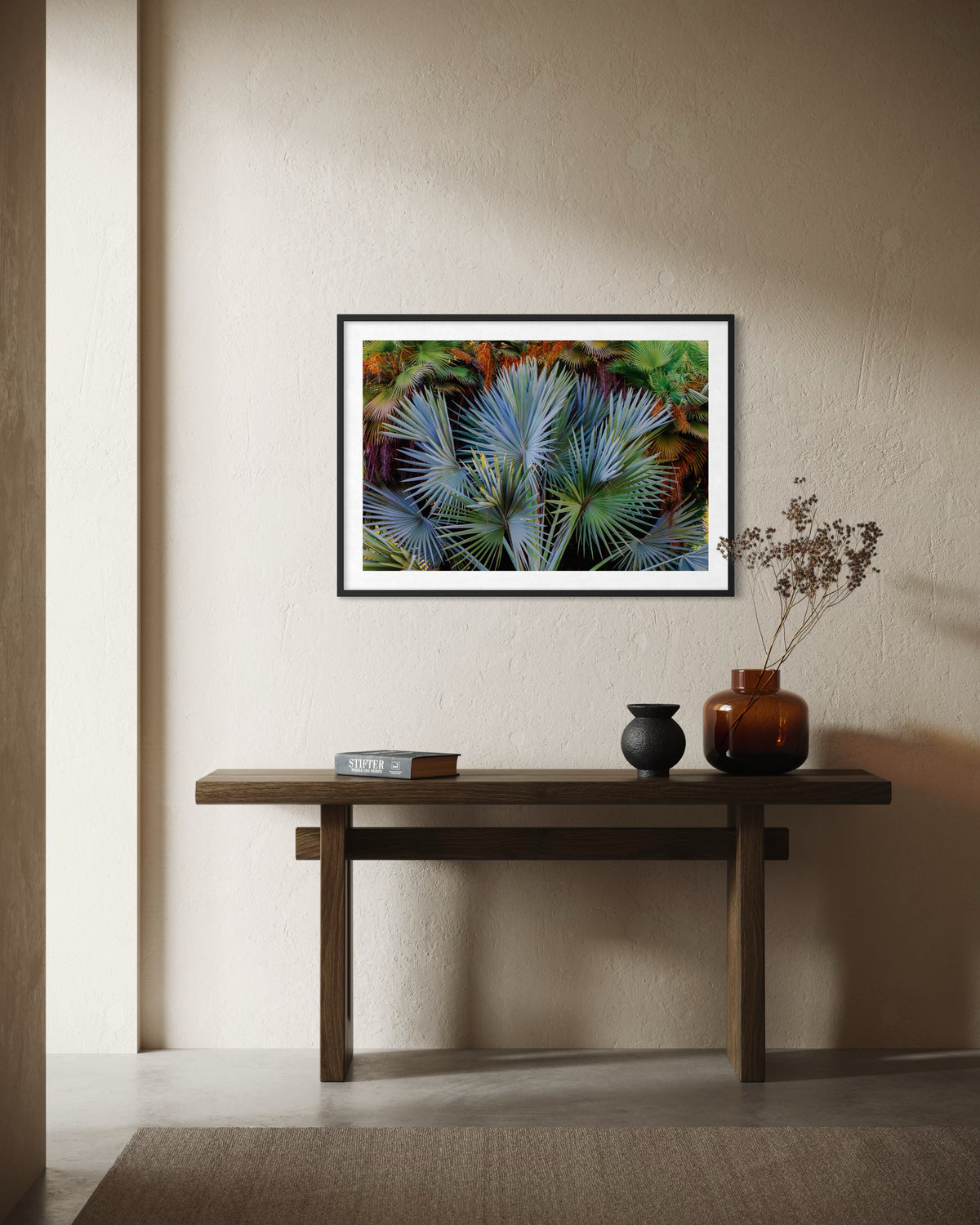Framed Footstool Palm print hangs above a wooden table with two vases and a book against a beige wall.