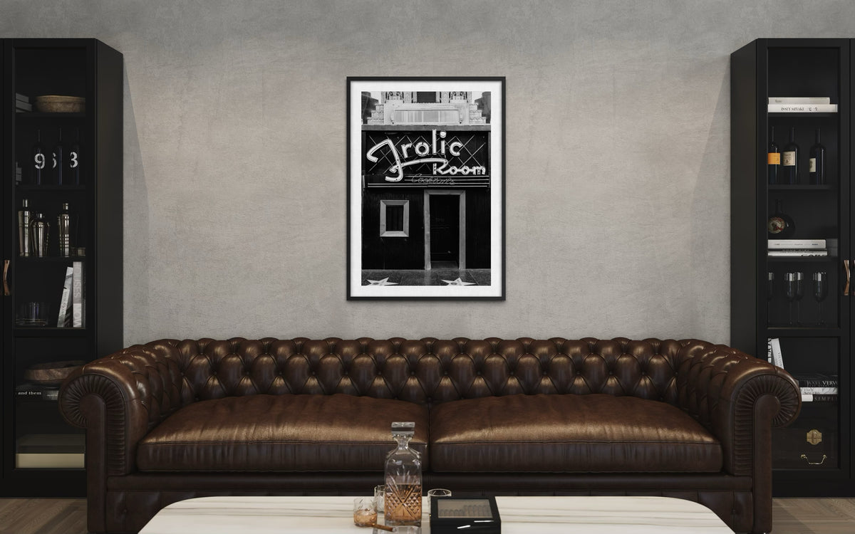 Framed Frolic Room print from Hollywood hangs above a brown leather sofa and white coffee table.