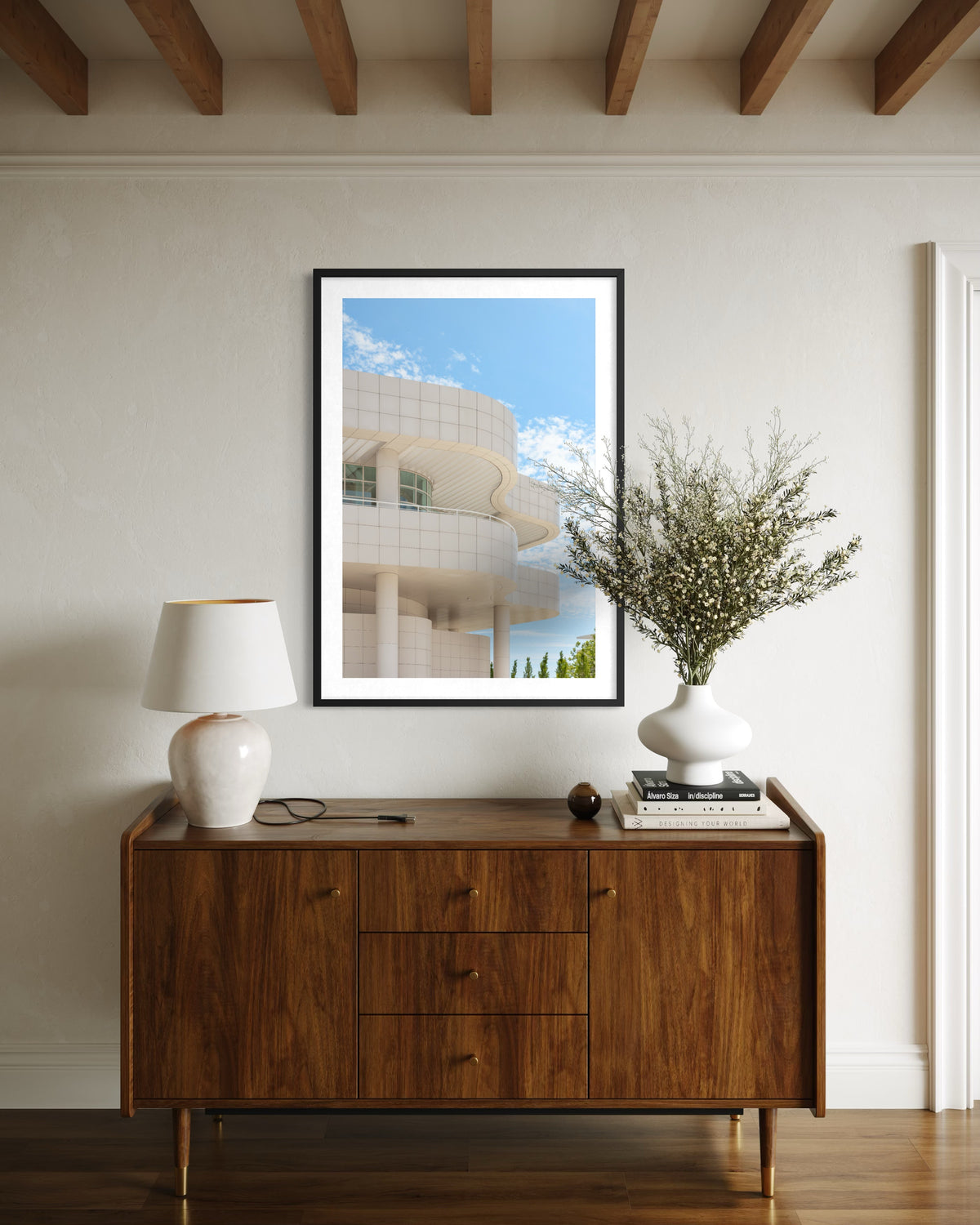 Wooden sideboard with lamp, books, and vase below Getty Center I photo on white wall in Los Angeles.