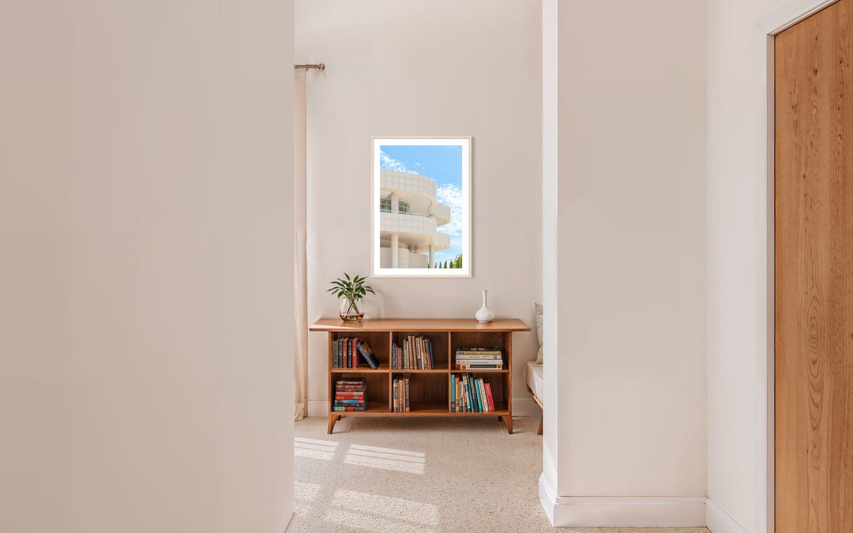 Small bookshelf and plant in a hallway; framed abstract Getty Center I Los Angeles photo hangs on the wall.