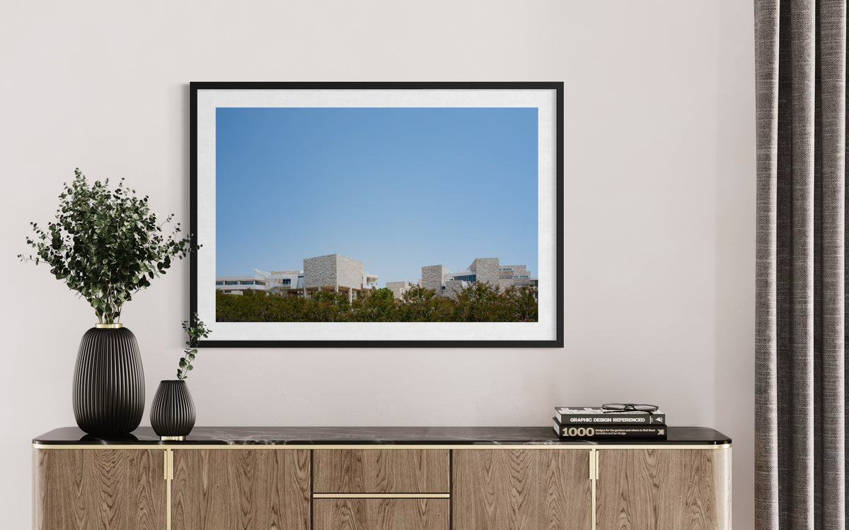 Framed print of modern travertine architecture at the Getty Center, Los Angeles, above a wooden console with vases.