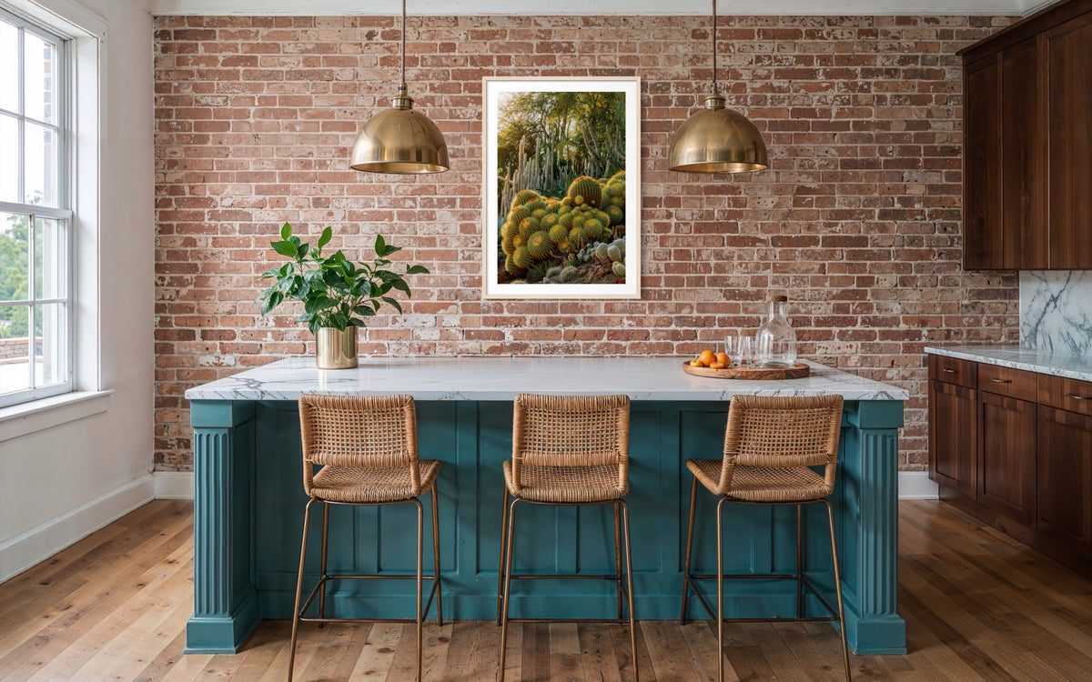 Kitchen with a brick wall, teal island, rattan stools, gold pendant lights, and cactus art above the counter.