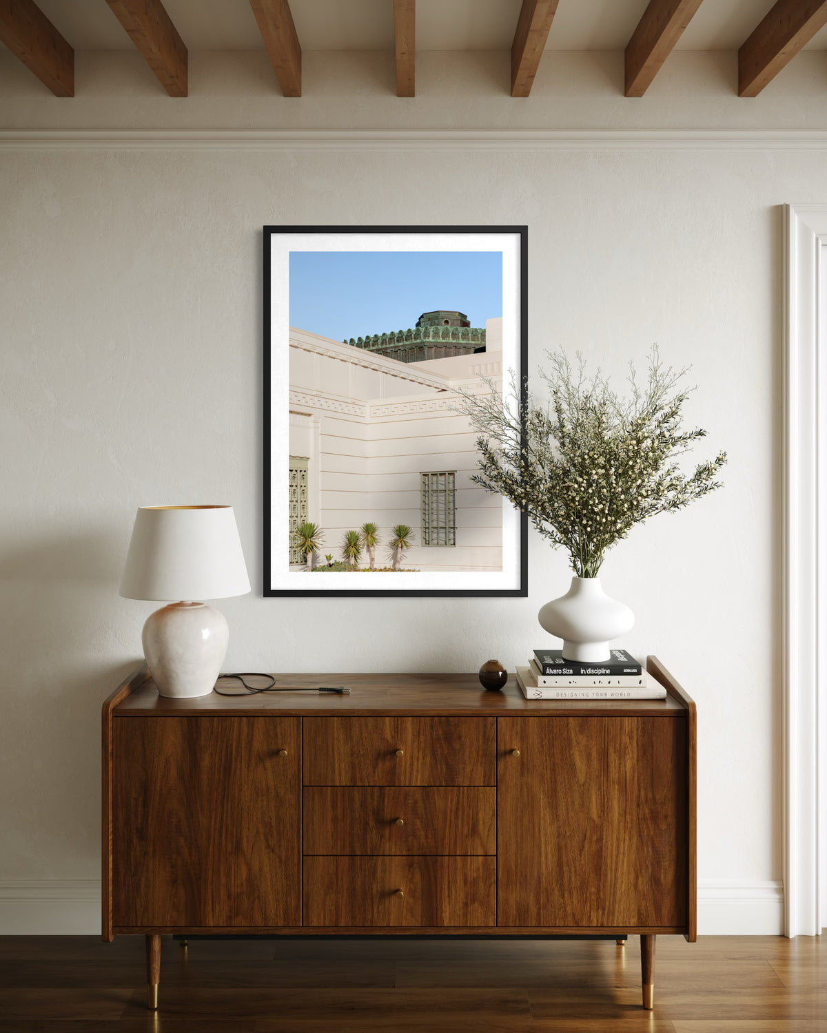 Art Deco “Griffith Observatory Moment” print on wall above a wooden sideboard with lamp, vase, and books.
