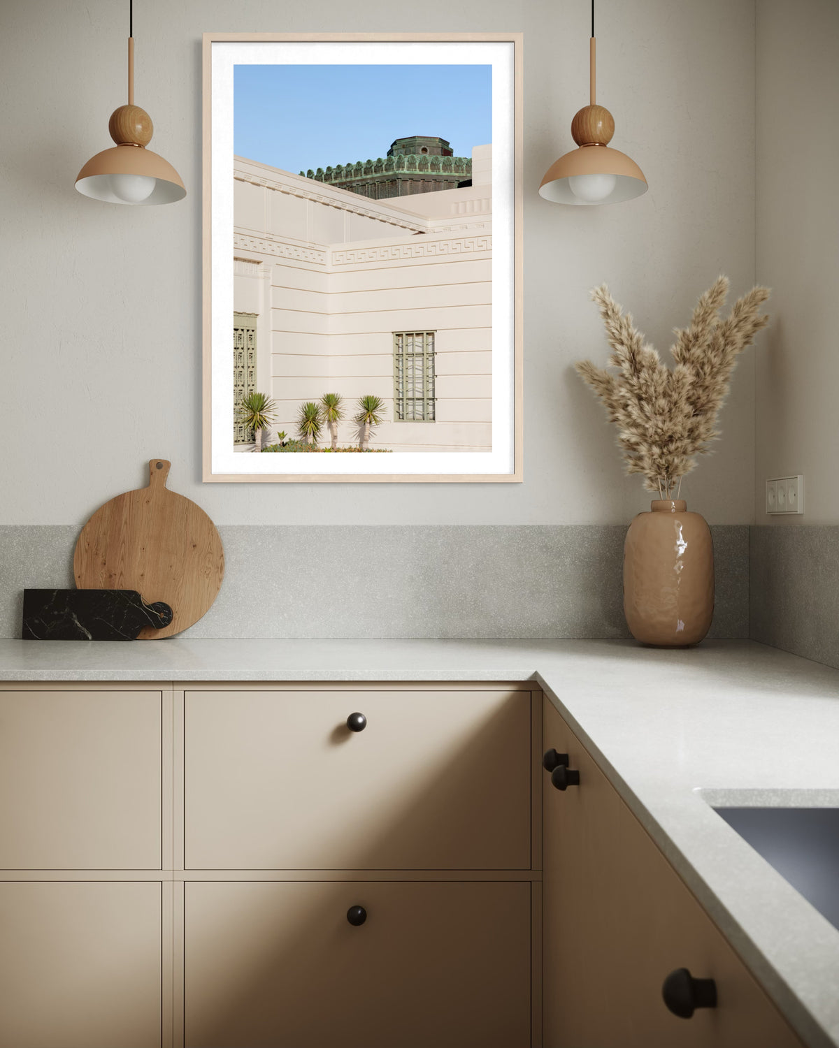 Beige kitchen with marble counter, framed Griffith Observatory art, pampas in vase, and pendant lighting.