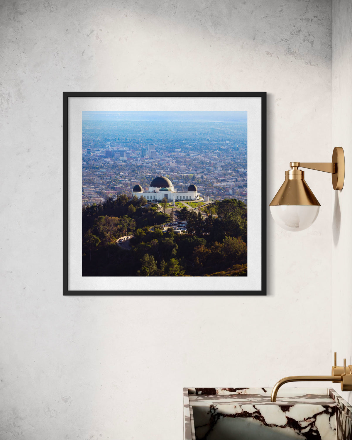Framed Griffith Observatory photo on wall above marble sink with gold sconce, Los Angeles location.