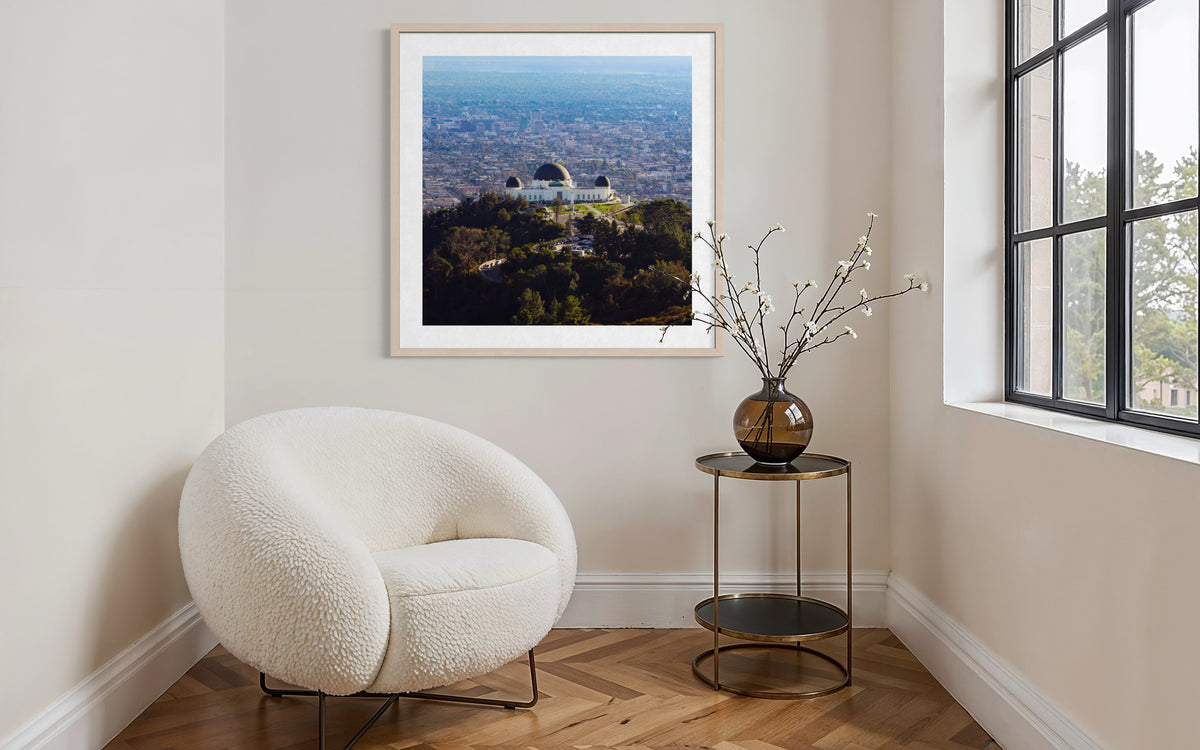 White chair and side table by window with framed Griffith Observatory print in a modern Los Angeles room.