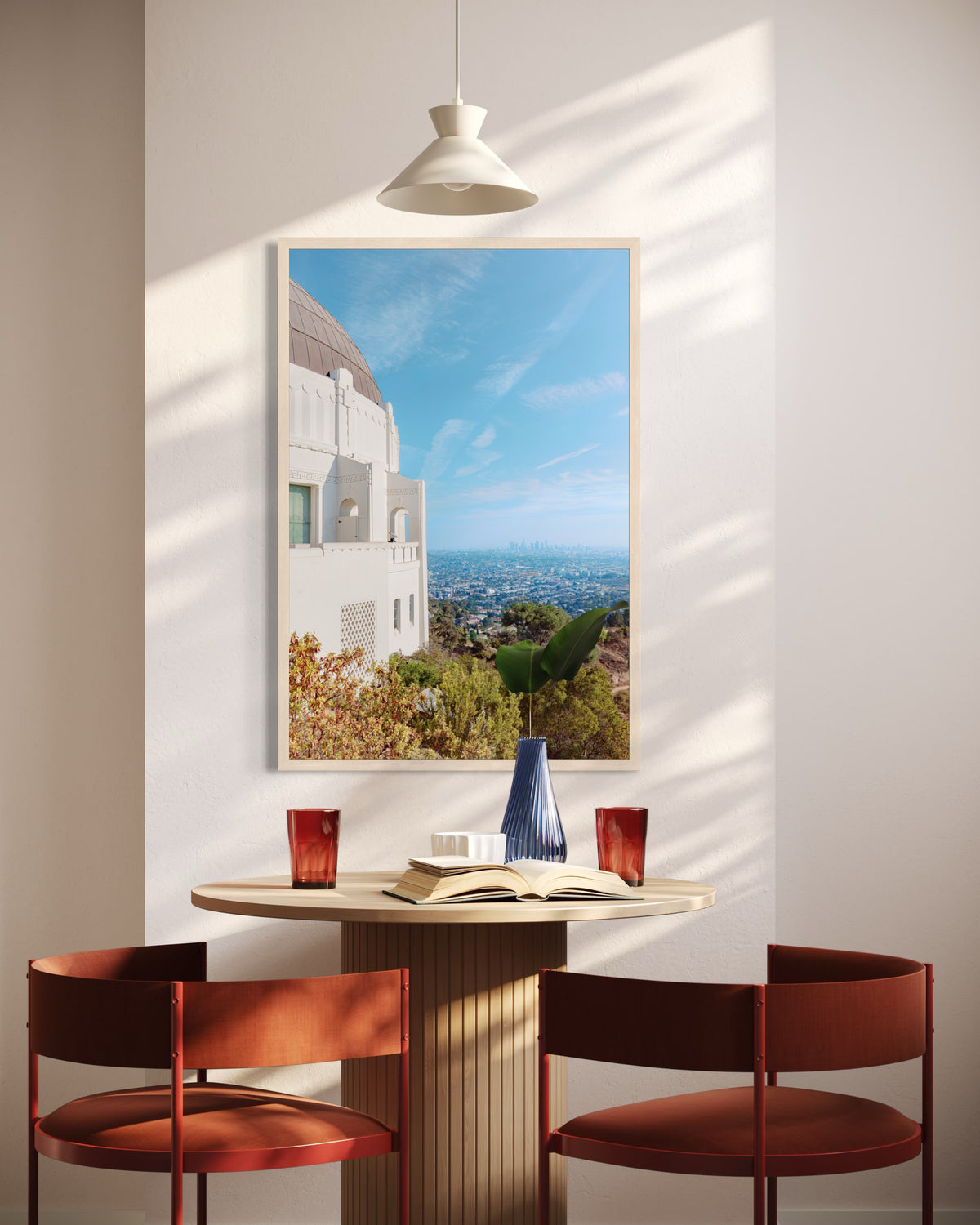 Round table with two red chairs, books, and Griffith Observatory View art print on the wall in a Los Angeles room.
