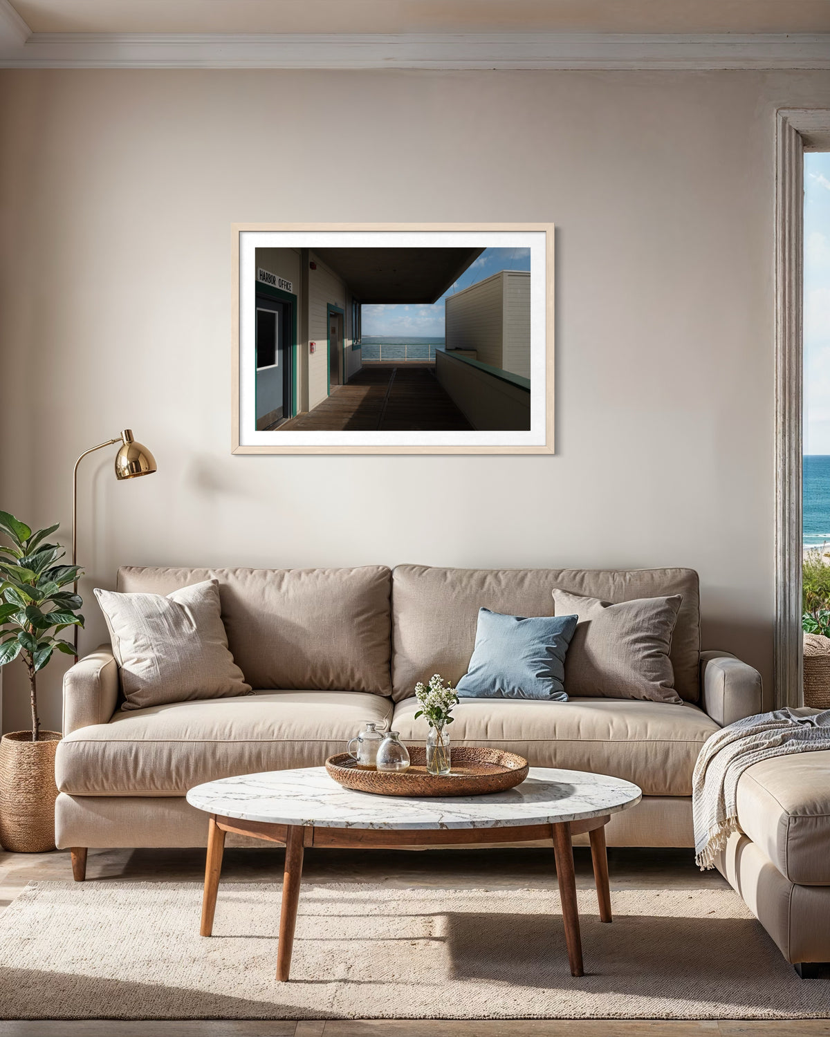 Beige sofa with blue pillows faces round coffee table, ocean visible through window near Santa Monica Pier.