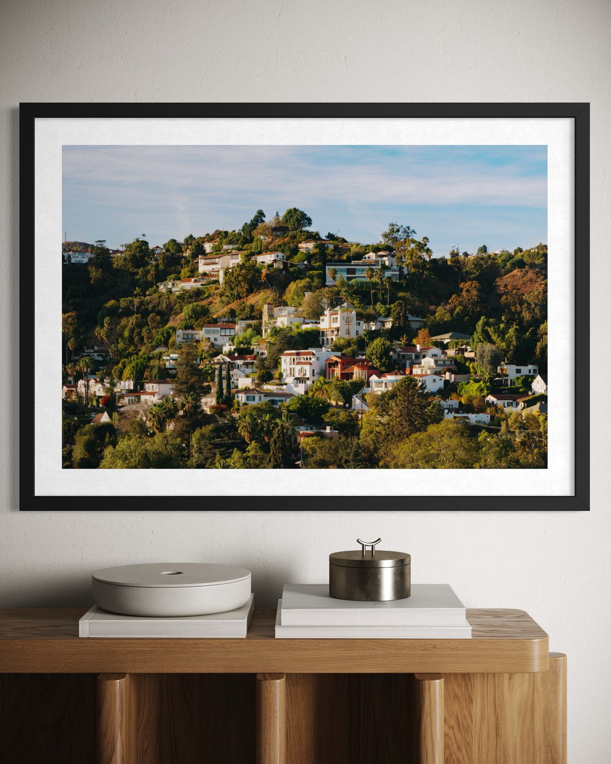 Framed Hollywood Hills photograph above a wooden sideboard with decorative objects in a modern room setting.