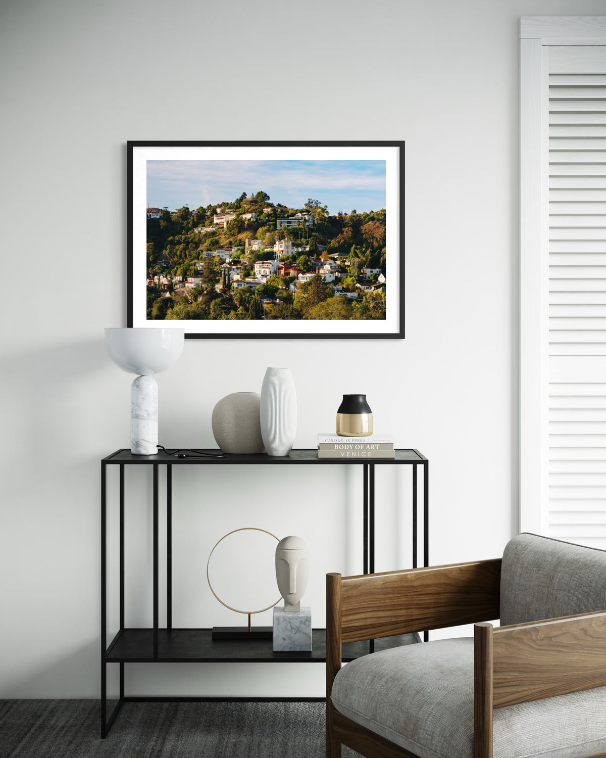 Framed photograph of the Hollywood Hills displayed above a modern console with vases in a minimal living room.