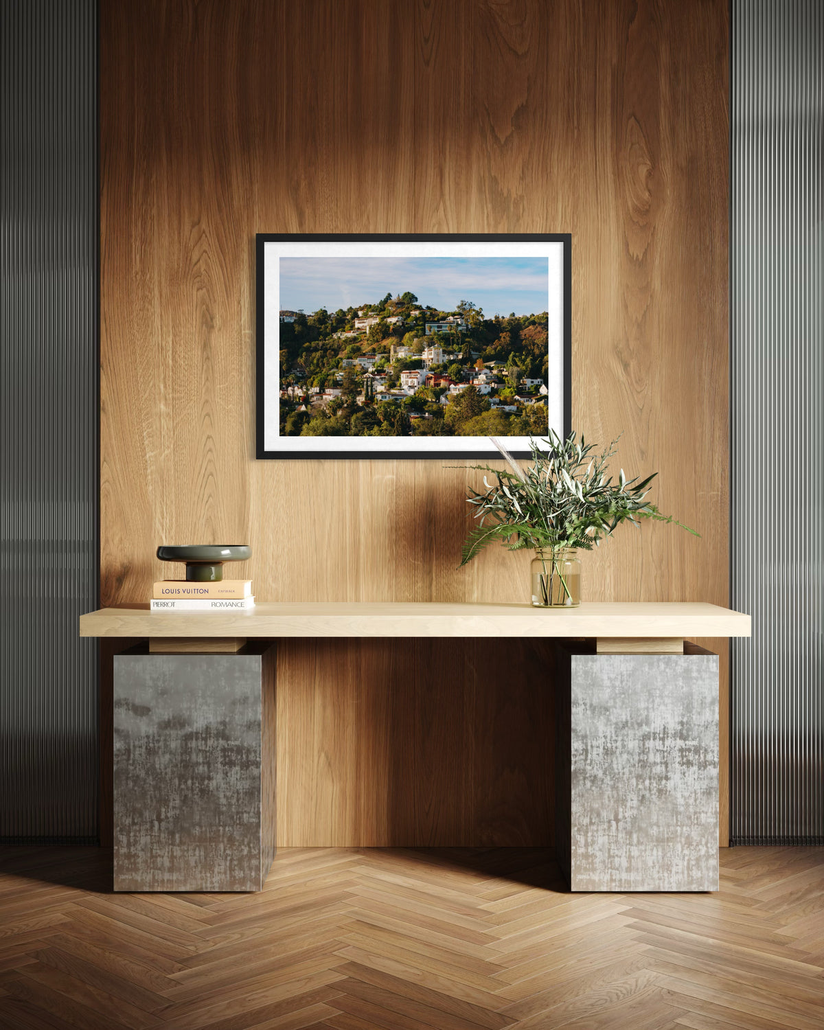 Console table with books and vase beneath a Hollywood Hills photo on a wood-paneled wall in Los Angeles.