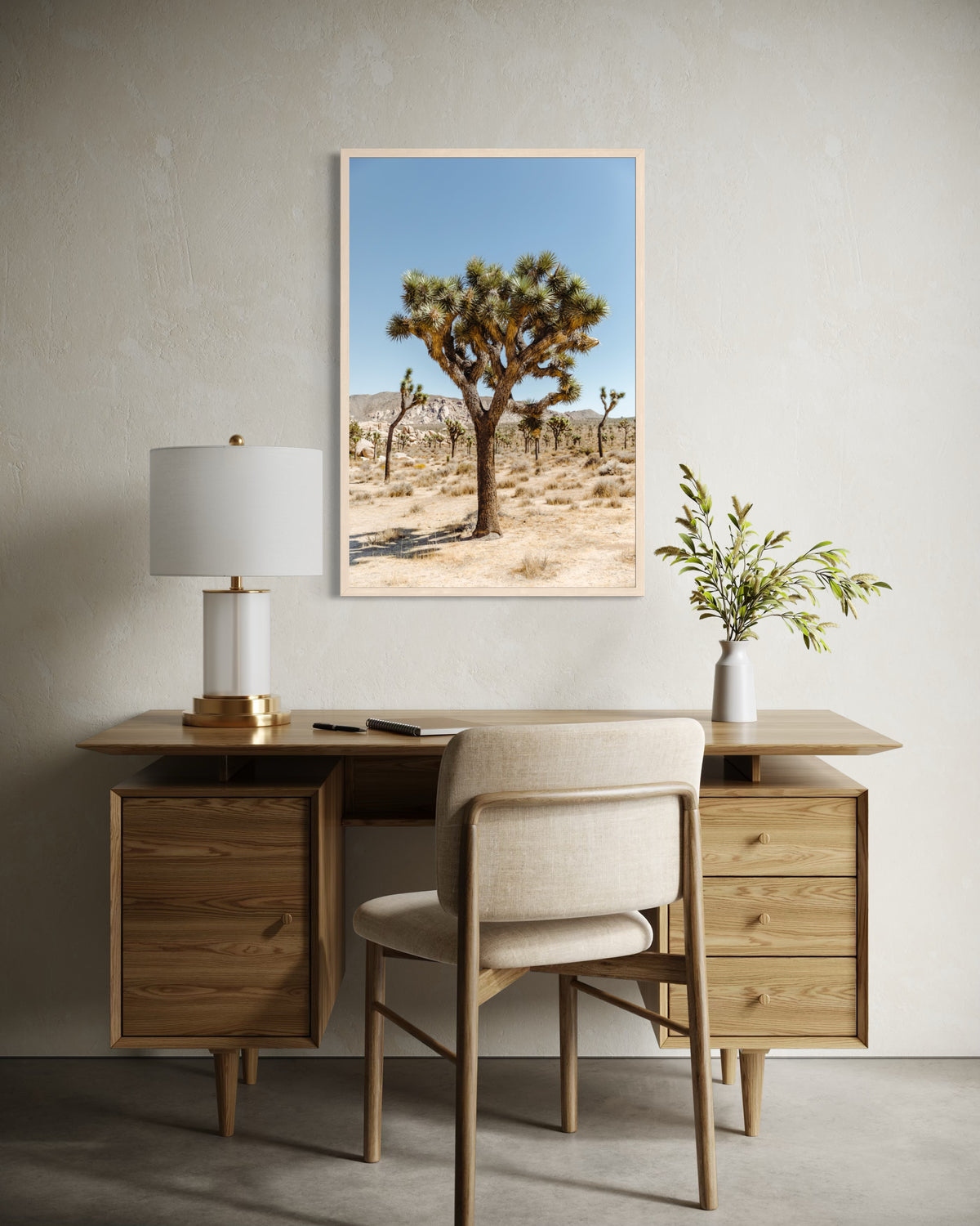 Framed “Joshua Tree I” landscape photograph on beige wall above desk with chair, lamp, and plant.