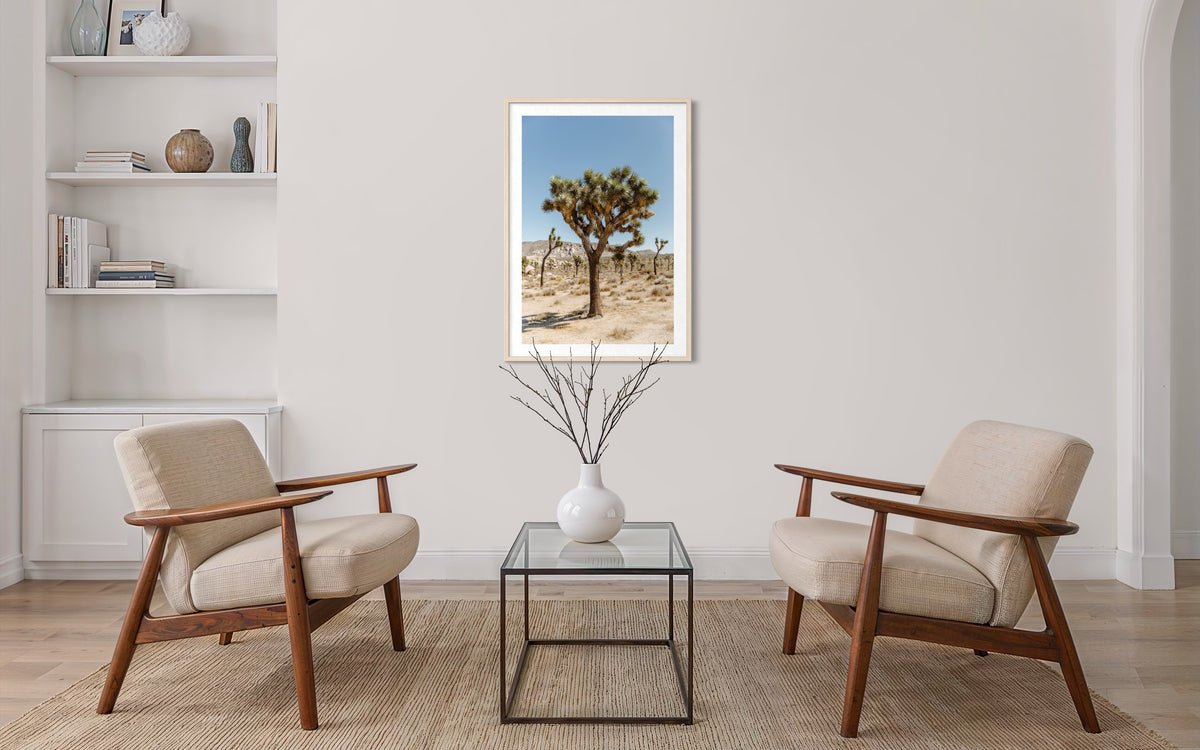 Minimalist living room with two beige chairs, glass coffee table, and Joshua Tree I artwork on the wall.