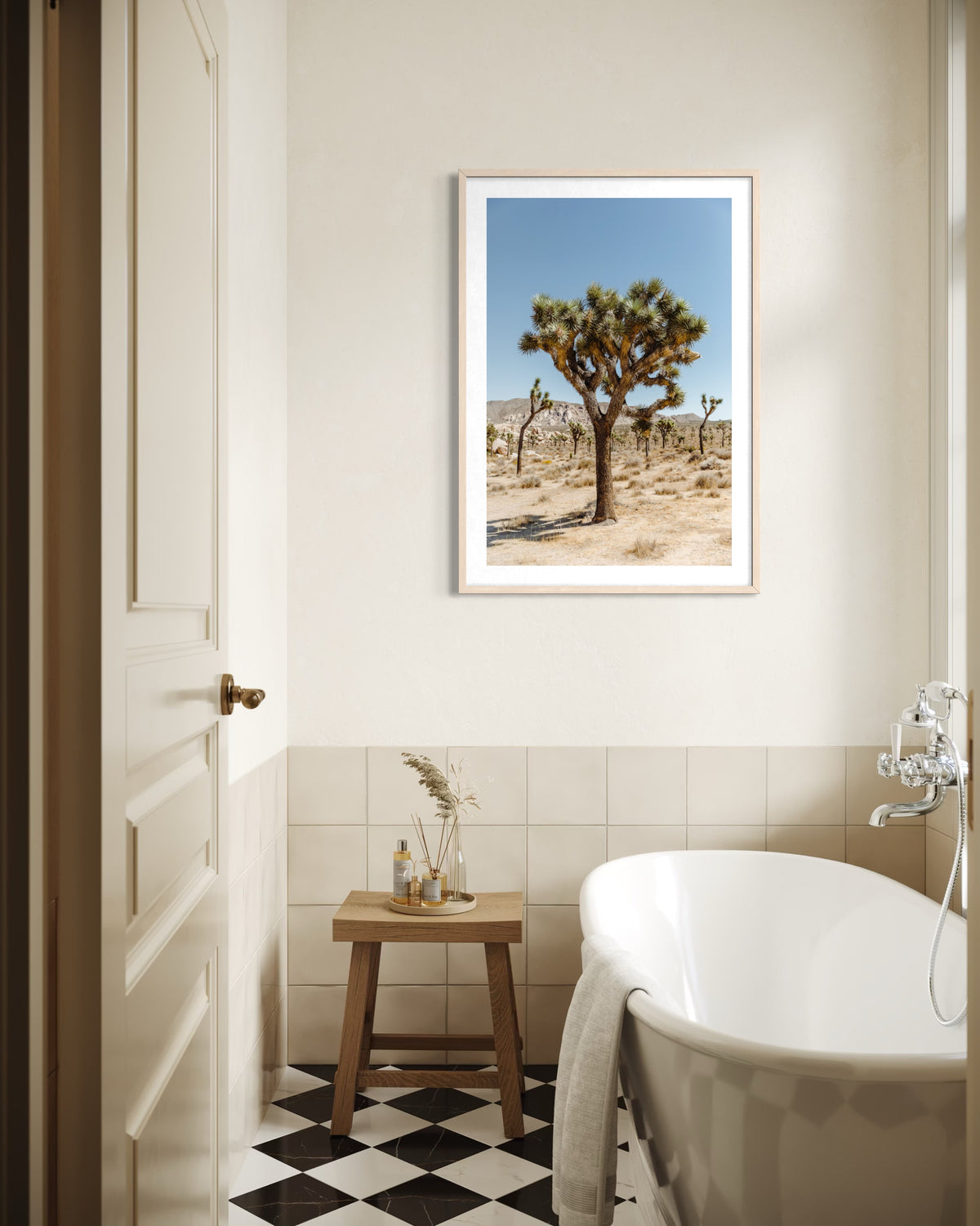 Bathroom with bathtub, wooden stool, and framed Joshua Tree landscape on the wall.