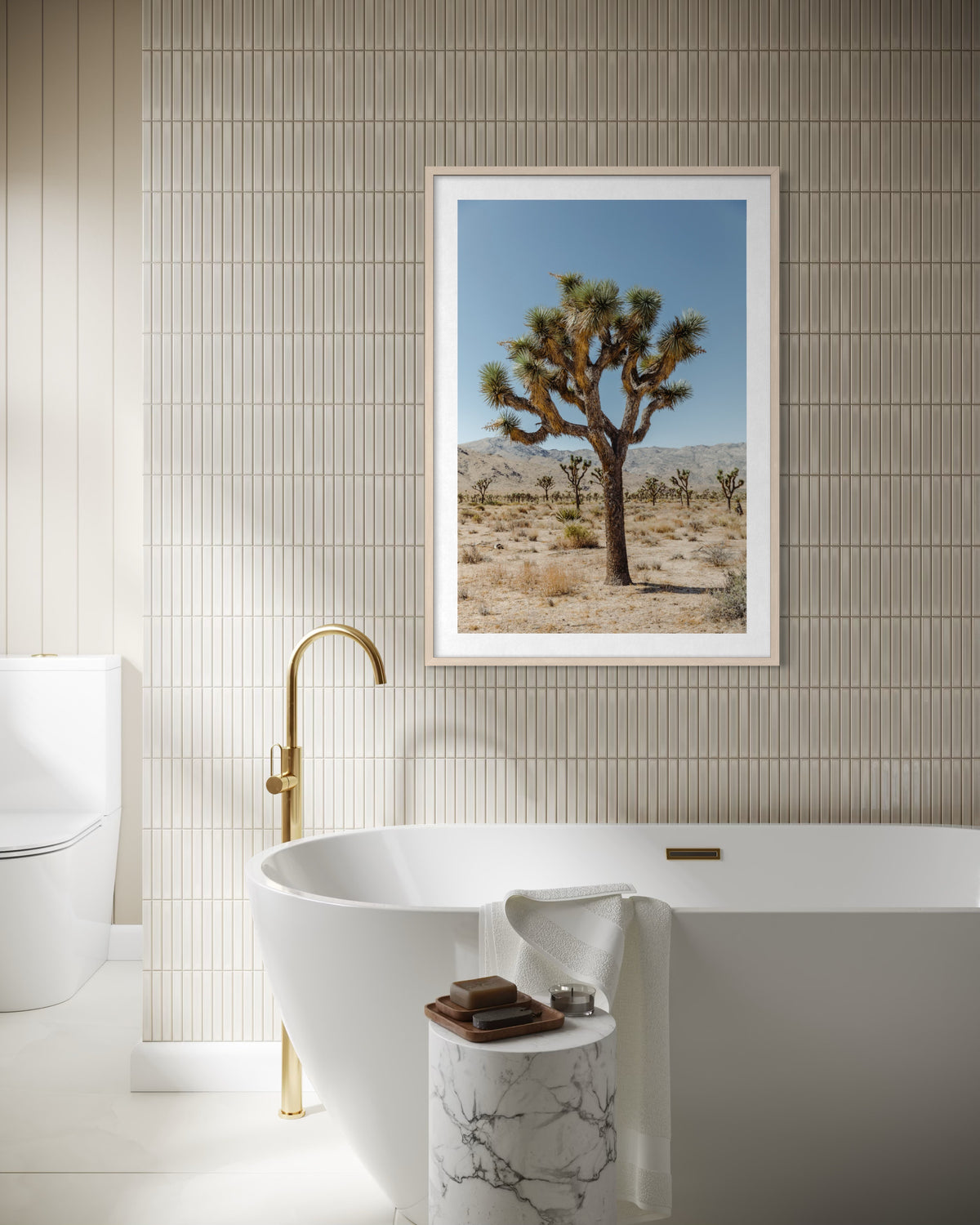 Freestanding tub with gold faucet below “Joshua Tree III” photography; bathroom interior setting.
