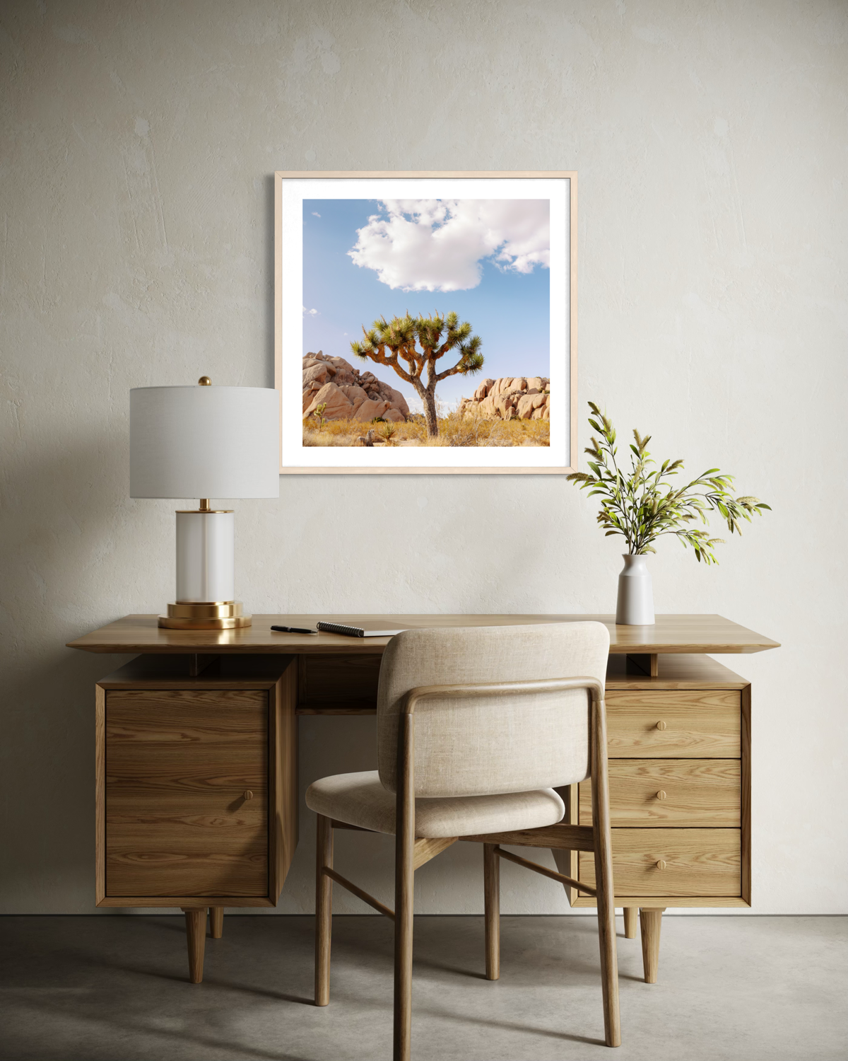 Framed “Joshua Tree IV” art above a wood desk with chair, lamp, and plant against a beige wall.