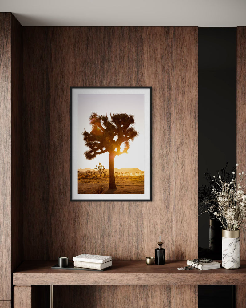 Framed print of a sunset over Joshua Tree desert, photographed in California, shown above a modern desk.