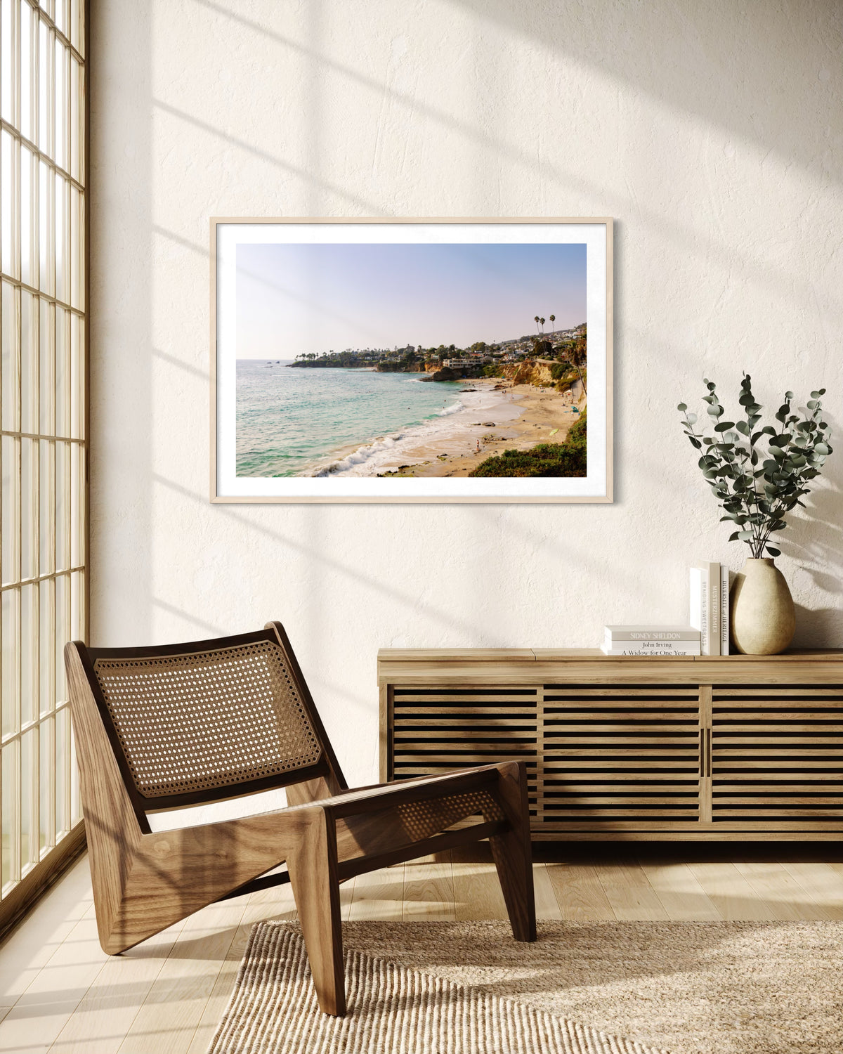 Chair and console with a vase beneath framed Laguna Beach View photo in a bright, airy coastal room.