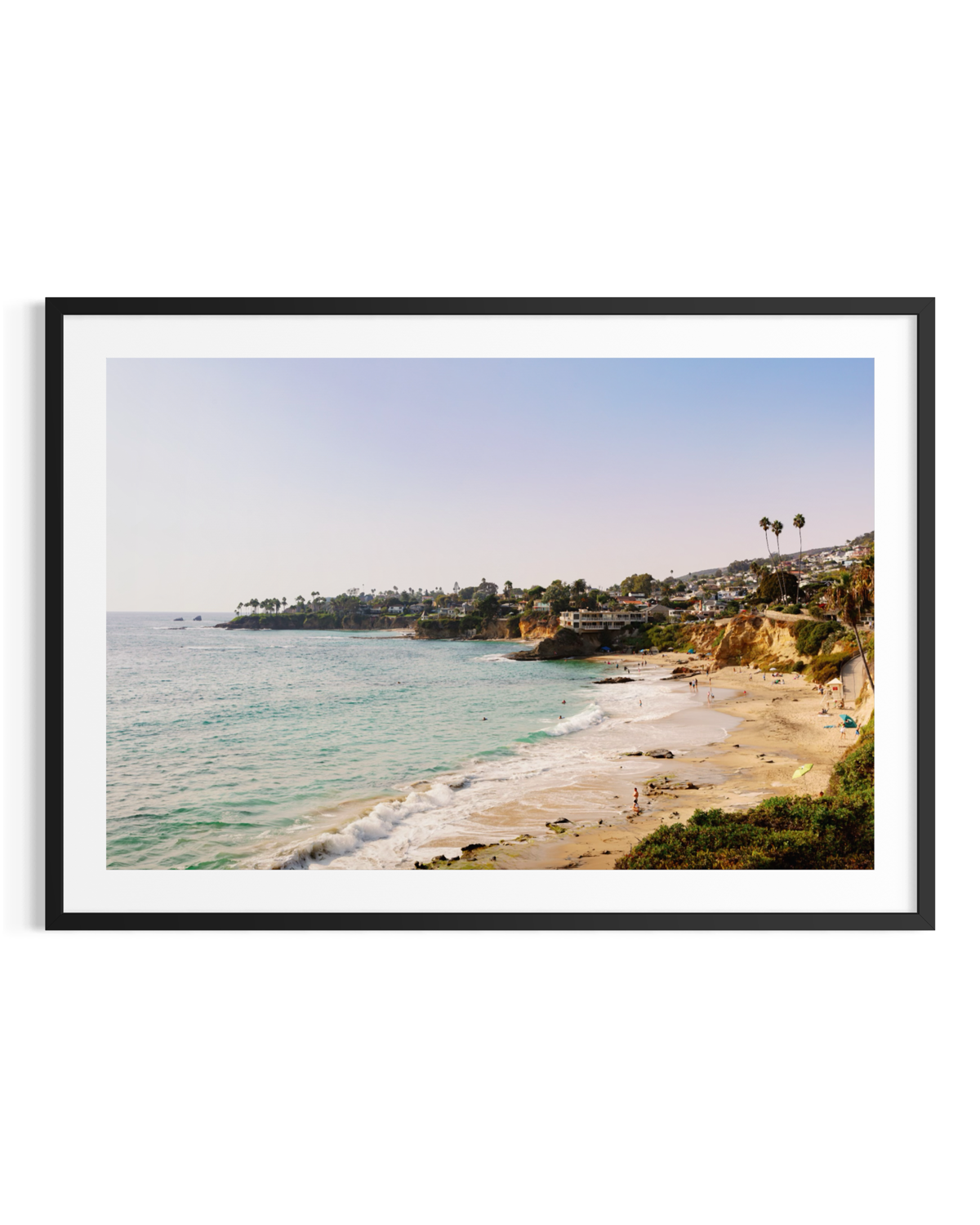 Black-and-white view of Laguna Beach with waves, rocky coves, cliffs, and houses beneath a clear sky.