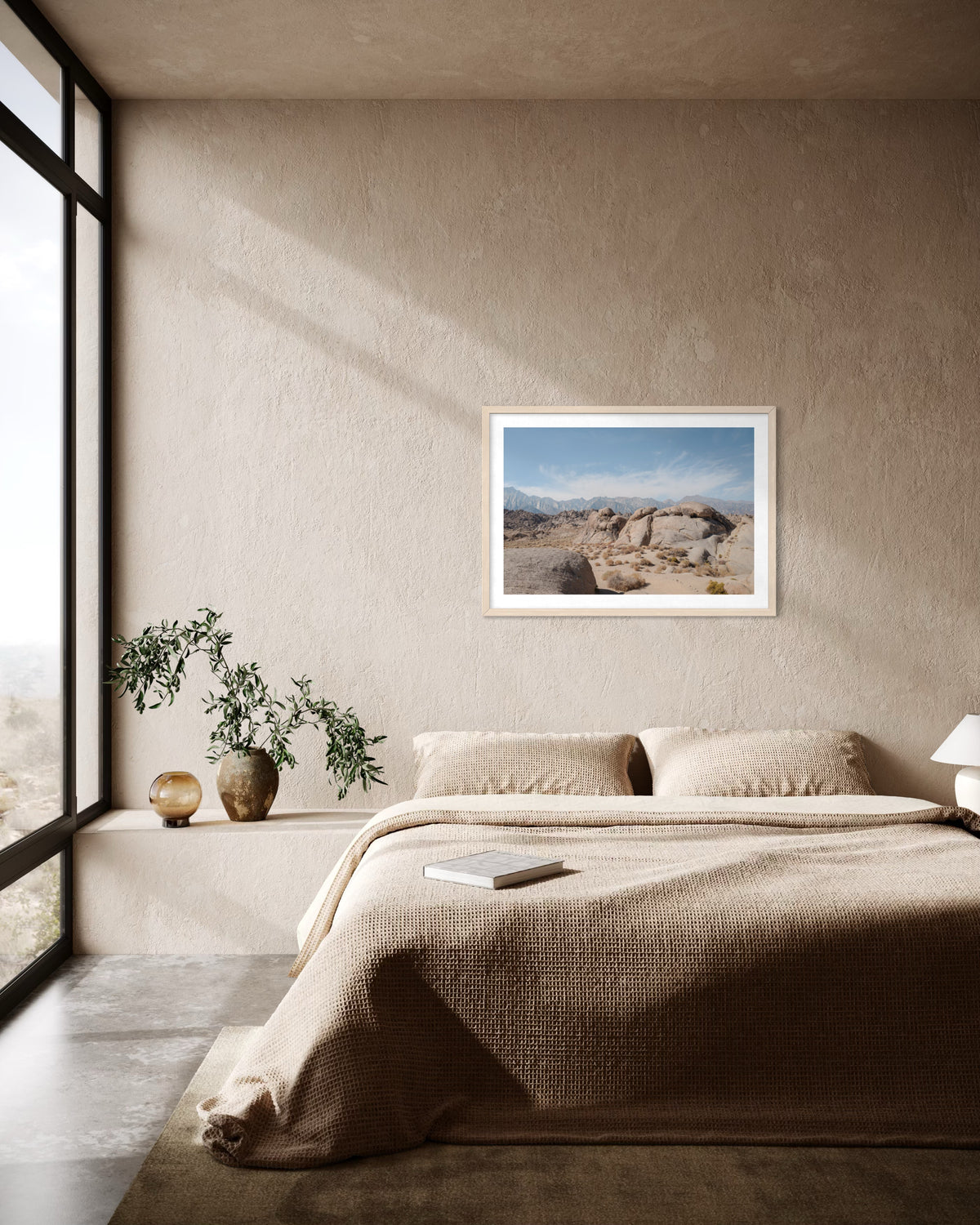 Beige bedding and potted plants in a bedroom; Lone Pine, California landscape photo hangs above the bed.