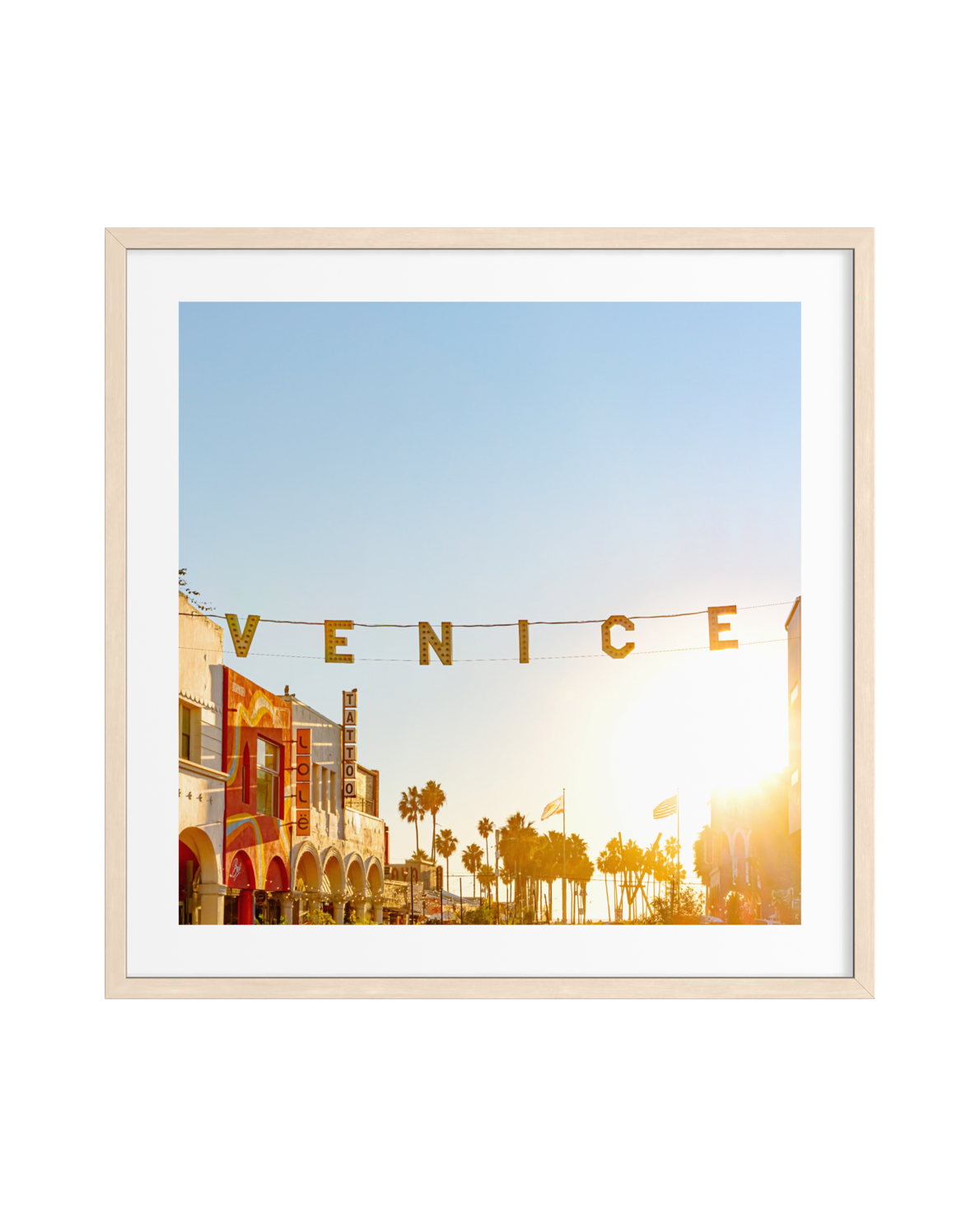 A sunlit sign over Venice streets and palm trees, photograph displayed in a light wood frame.