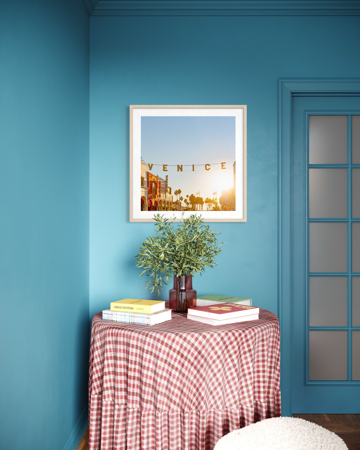Round table with books and plant by a blue wall displaying “Magic Hour in Venice” photo print.