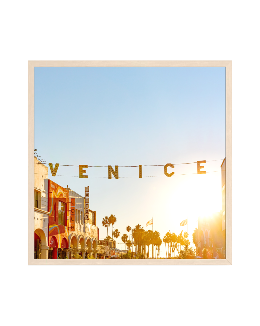 Neon sign glows above palm trees and colorful buildings at sunset in Venice, Los Angeles.