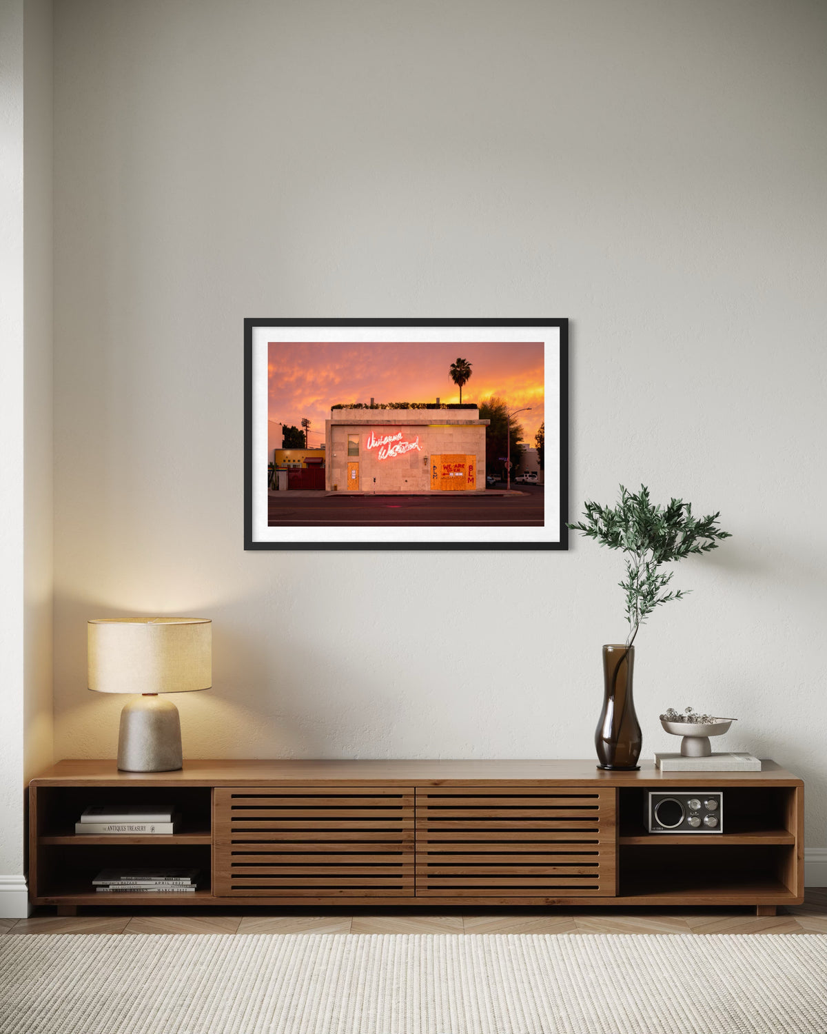 Framed “Melrose Avenue, the Summer of 2020” Los Angeles street photo above a console with lamp, books, and plant.