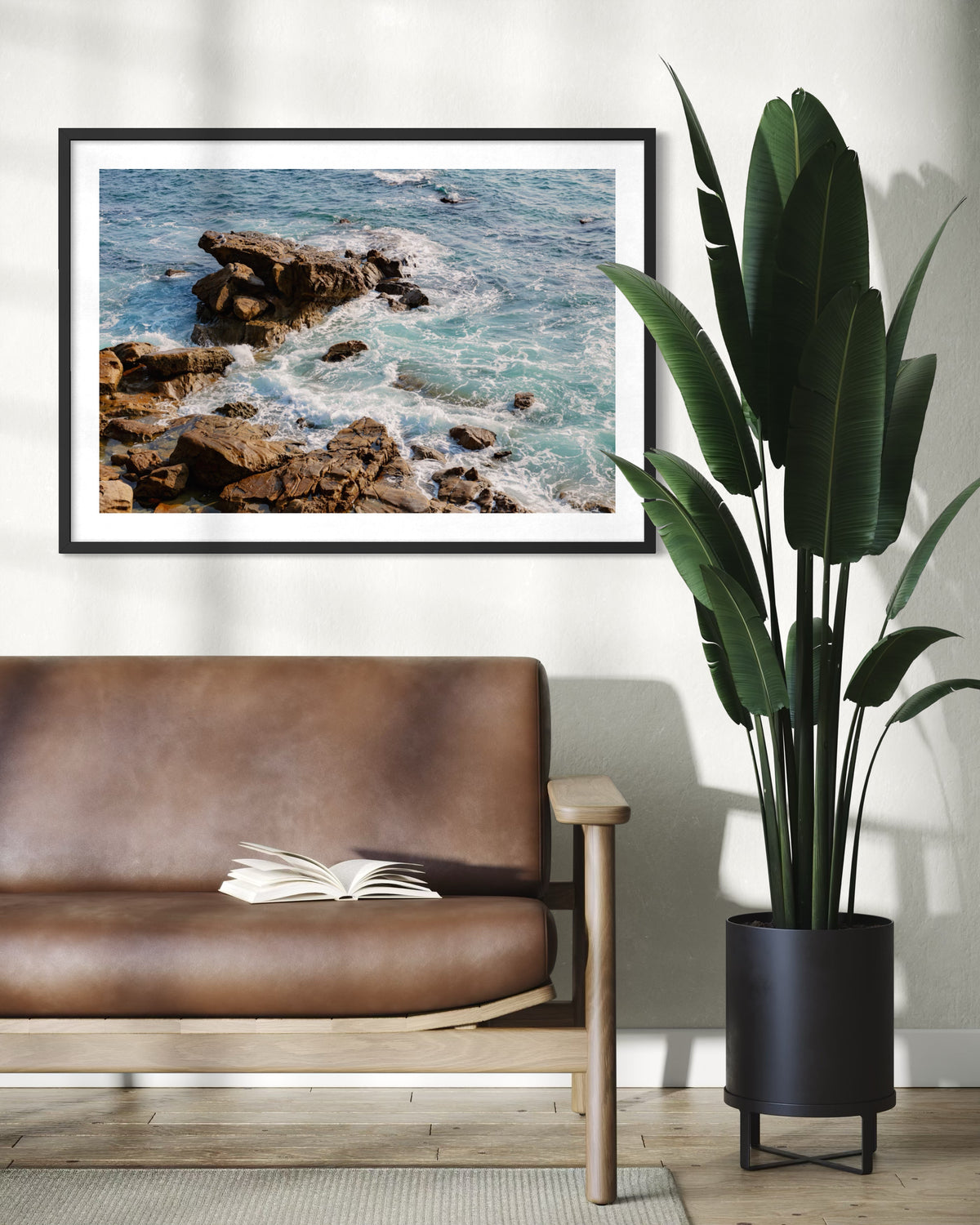 Brown leather sofa, open book, plant, and “Ocean Foam” beach print displayed in a bright living room.