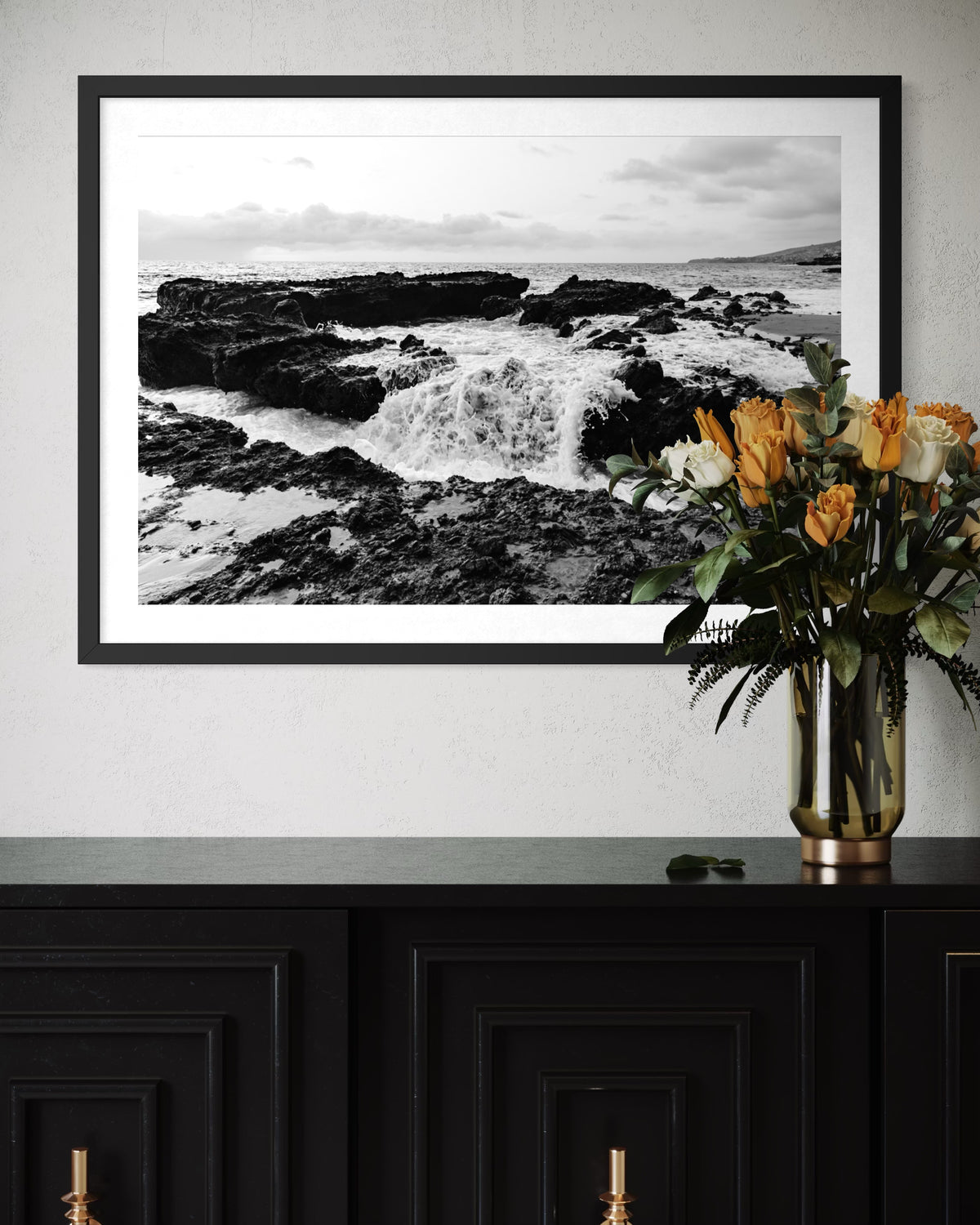 Black-and-white seascape print titled “Ocean Momentum” displayed above a black cabinet with yellow and white flowers.