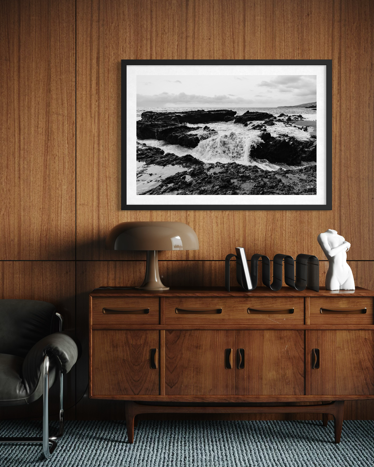 Framed “Ocean Momentum” black-and-white ocean print above a wood sideboard with books, lamp, and sculpture.