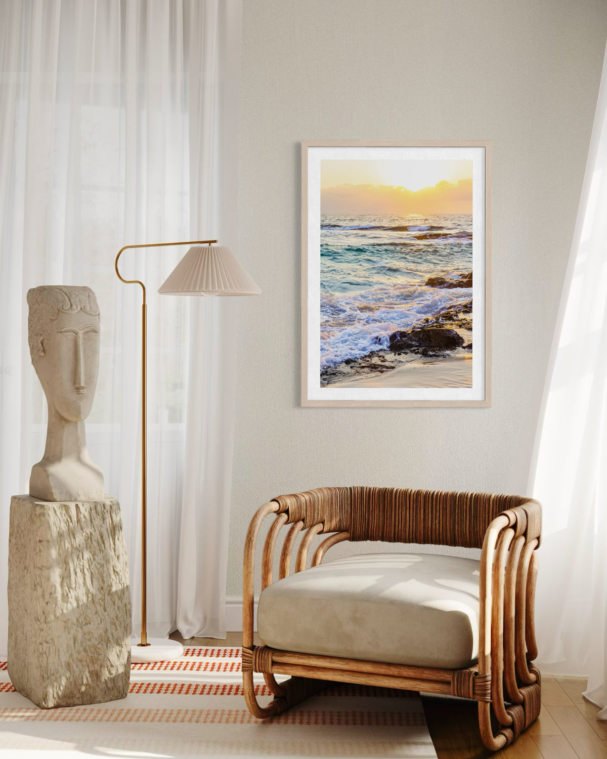Framed “Ocean Sunset” photograph on light wall above a wicker chair, lamp, and small sculpture in a room.