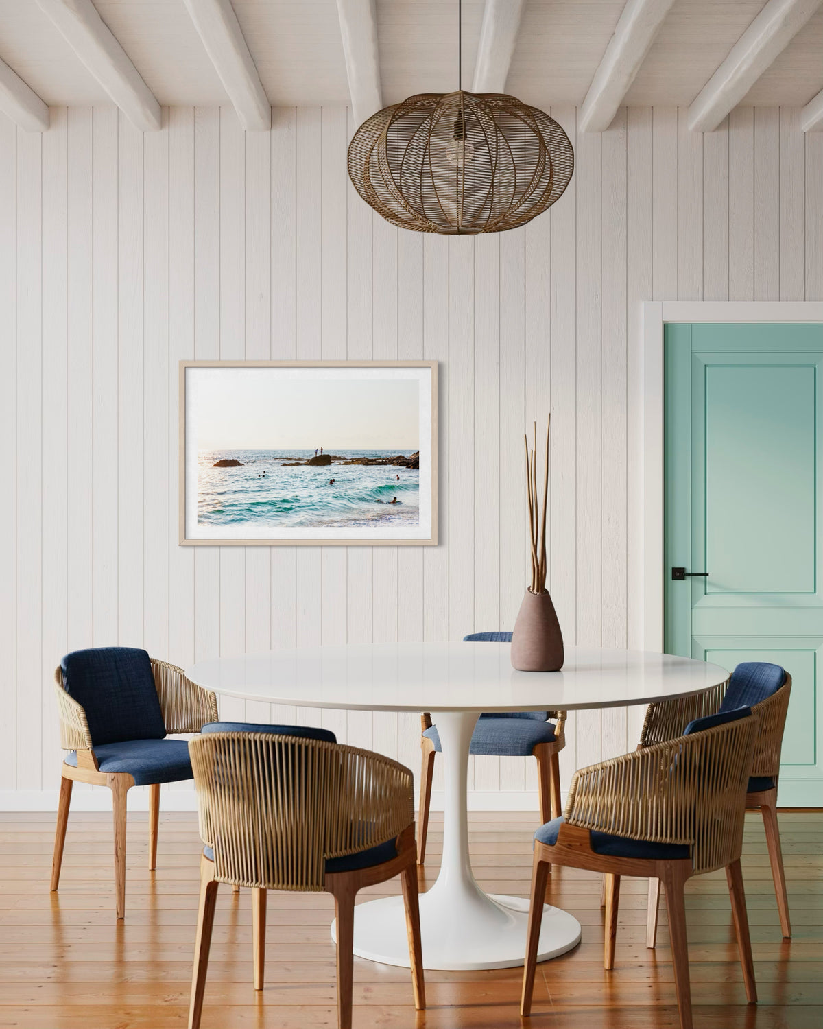 Ocean Swim photography print on wall beside a mint-green door, above a round table with wicker chairs.