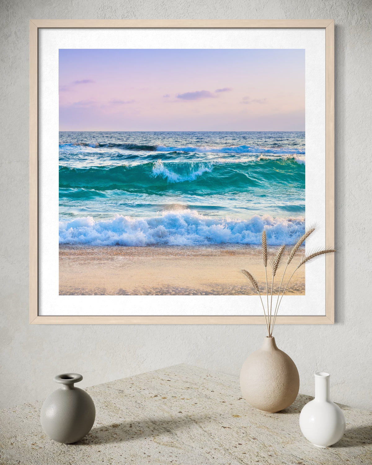 Ocean Waves II print of blue ocean waves on sand displayed above a table with three decorative vases.