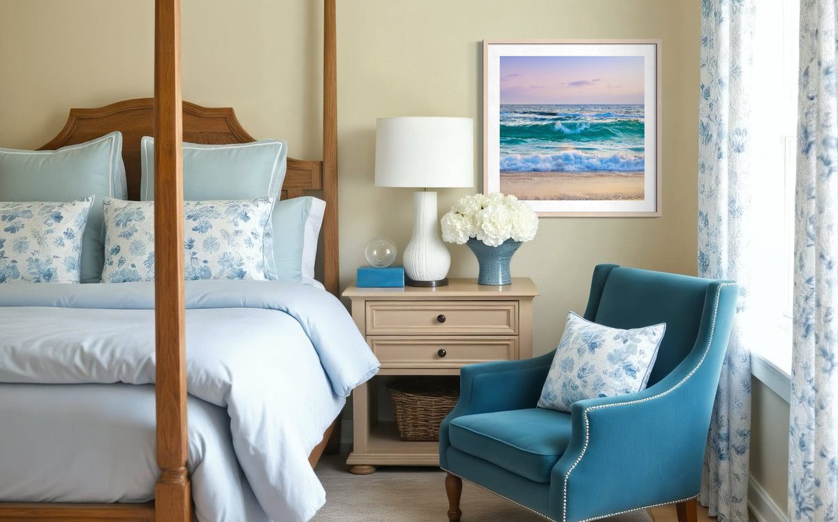 Blue and white bedroom with four-poster bed, armchair, floral accents, and Ocean Waves II artwork on the wall.