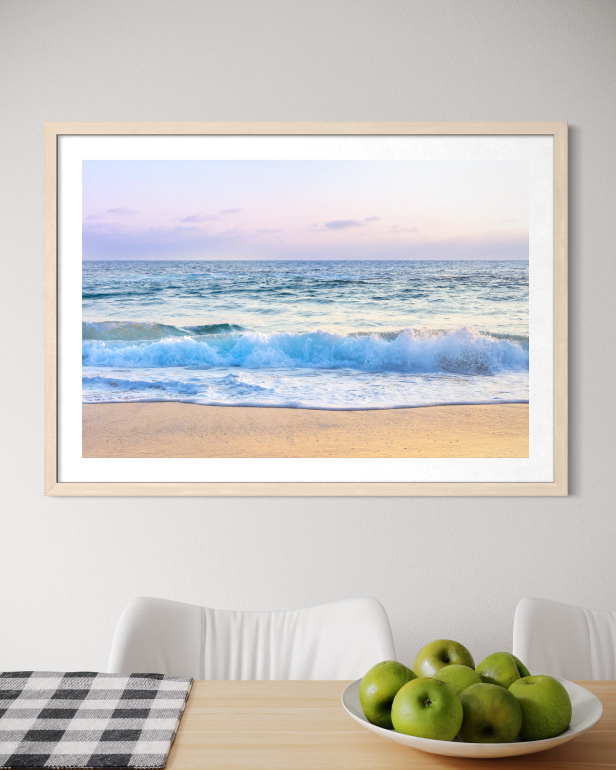 “Ocean Waves” framed print above a table with a white chair and a bowl of green apples in the room.